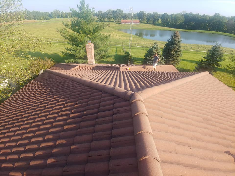 person inspecting a completed roof installation for a residential home, large pond and open field in background